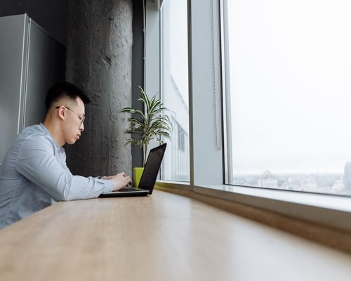 person working on a laptop beside a bright window